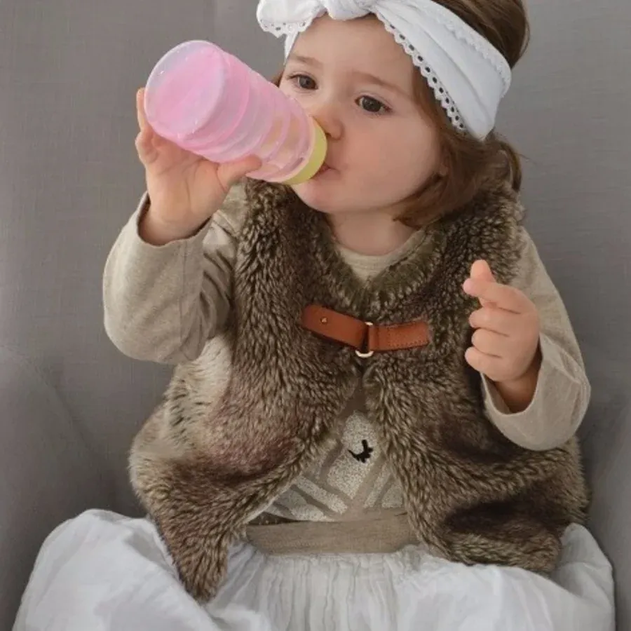 Une petite fille boit seule au biberon BIBEON rose