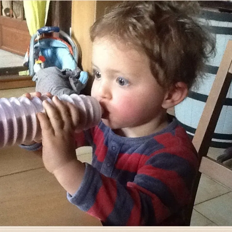 Un enfant tient le biberon BIBEON violet à deux mains, les doigts posés sur les soufflets