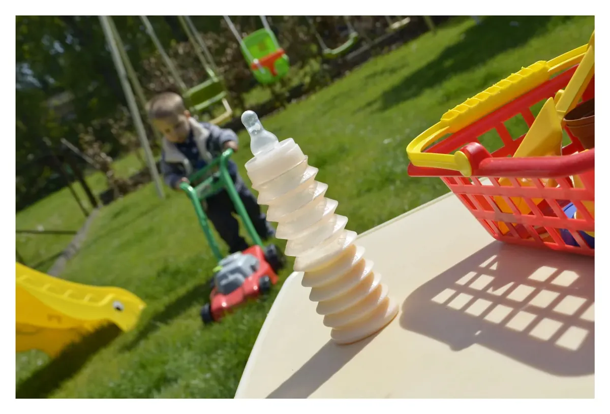 Un biberon BIBEON déplié posé sur une table de jardin, un enfant joue en arrière-plan